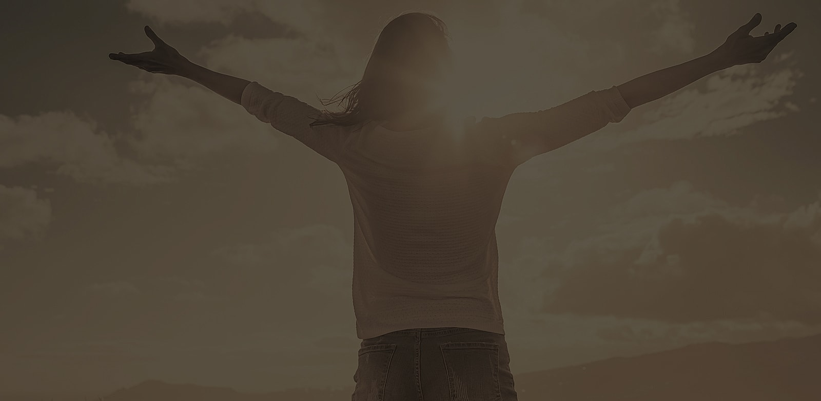 Person with outstretched arms against sunset backdrop.