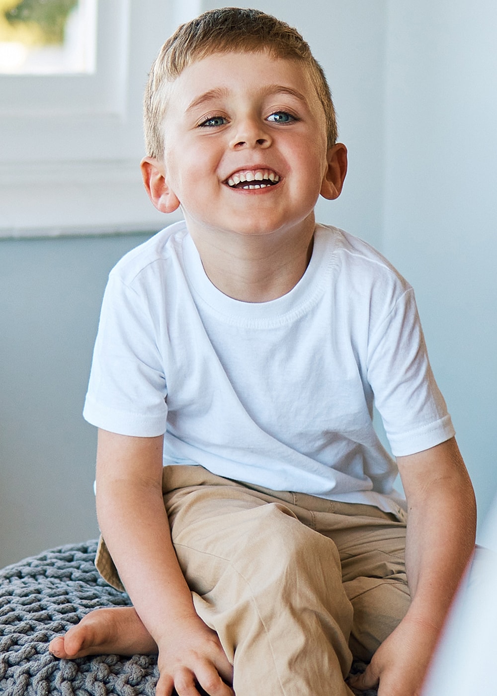 Smiling child sitting on a knitted pouf.