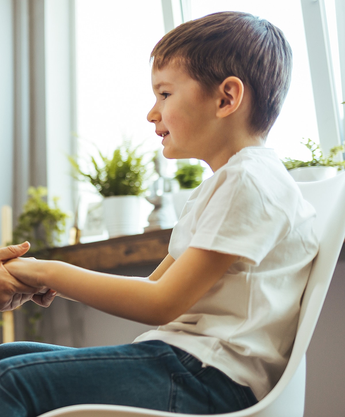 Child sitting, smiling, holding hands with adult.