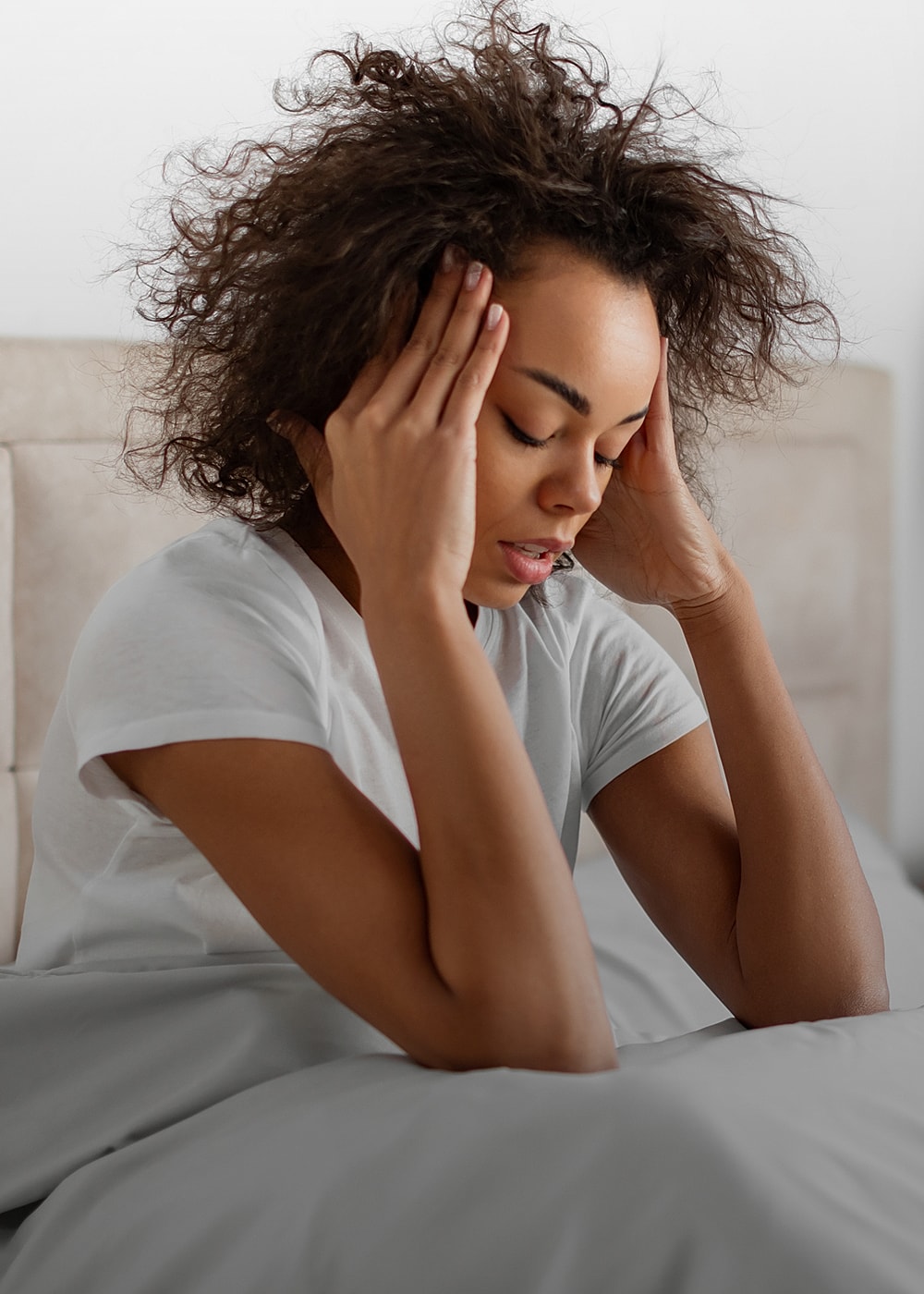 Woman with headache sitting on a bed.