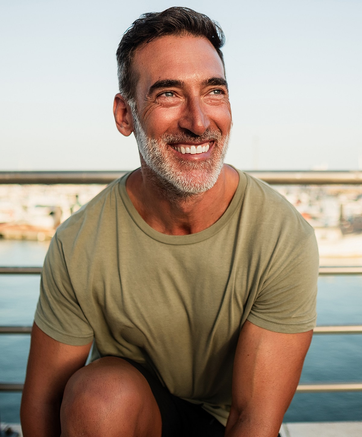 Smiling man sitting near water's edge.
