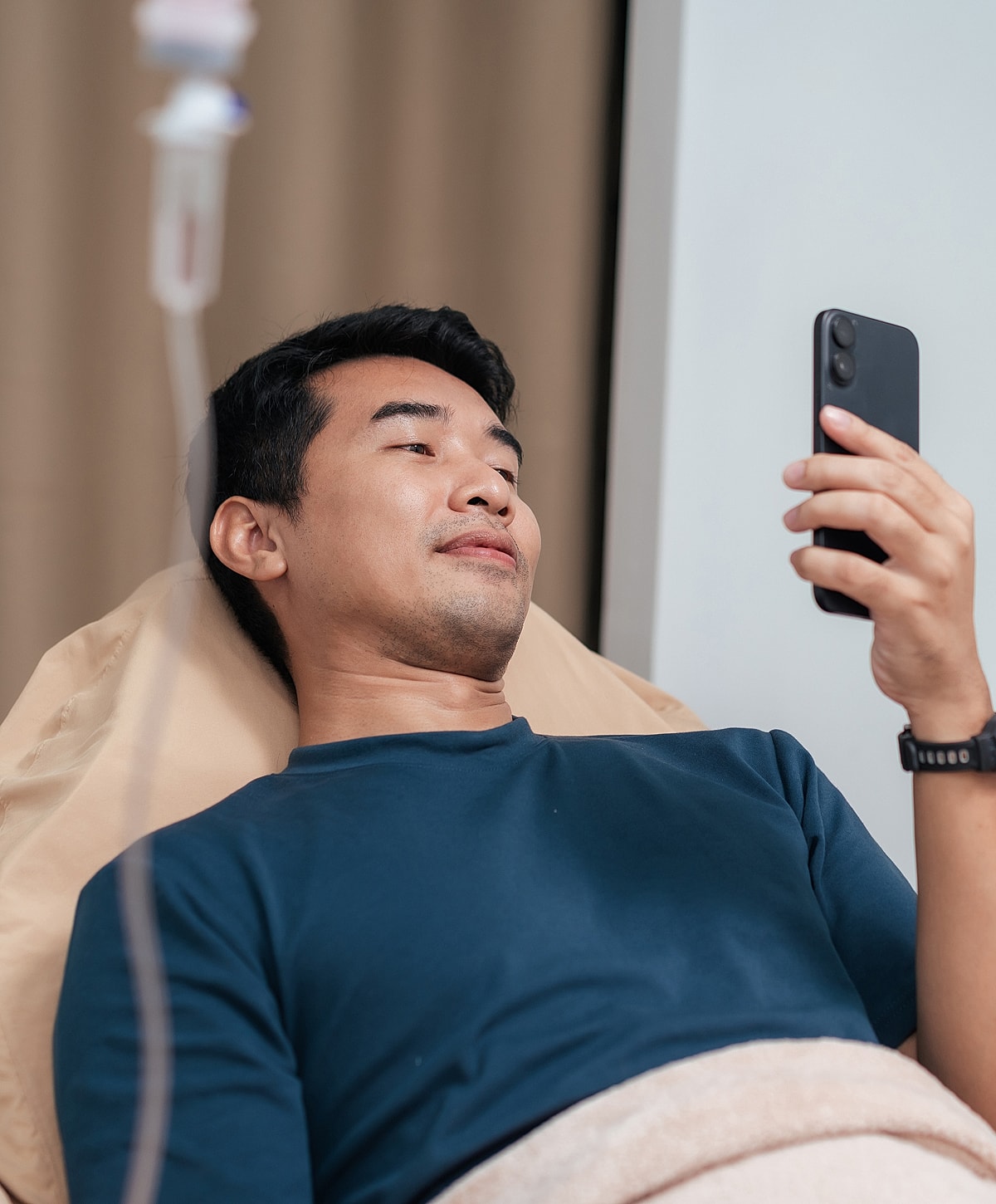 Man in bed using smartphone, IV drip nearby.