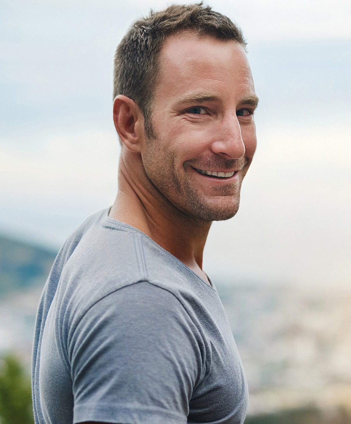 Smiling man outdoors in casual gray shirt.