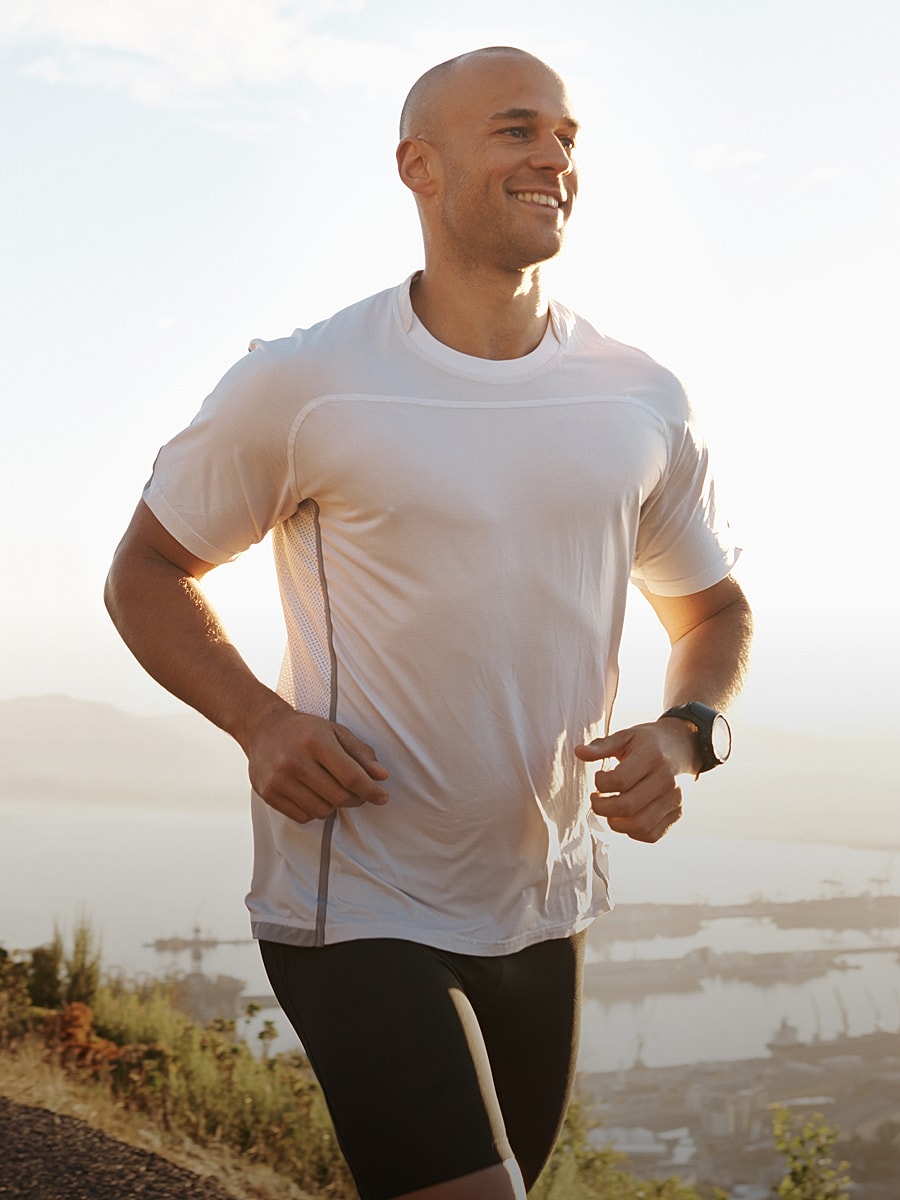 Smiling man jogging outdoors at sunrise.